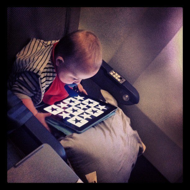 A baby is playing with an iPad while on an airplane.