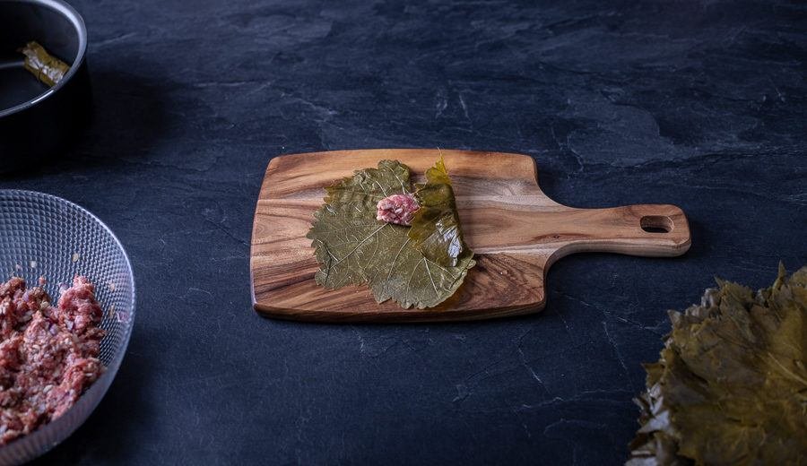 A wooden cutting board with Bulgarian foods, such as meat and leaves, on it.