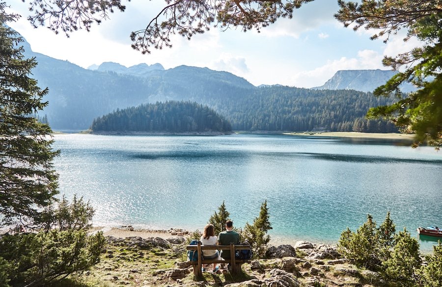 National Parks In Montenegro - A young couple sitting on a bench. Black lake. Durmitor