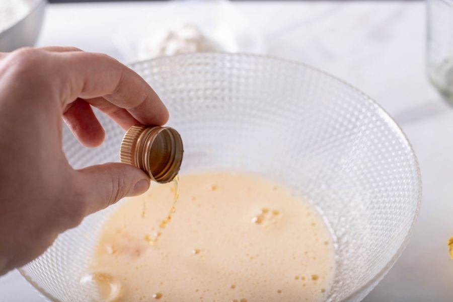 A person pouring a liquid into a bowl to prepare delicious Kroštule, traditional Croatian sweet pastry knots.