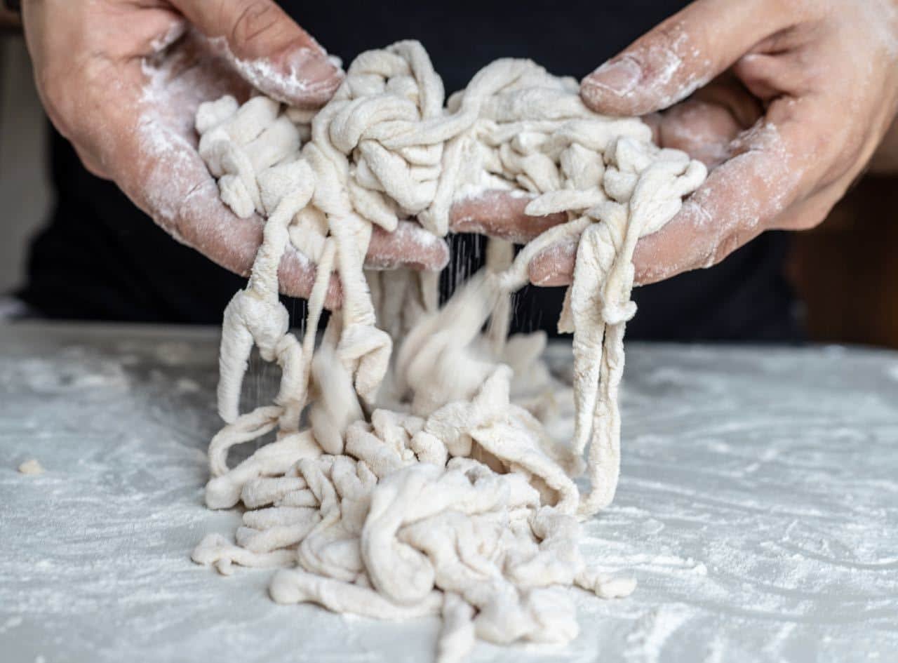 A person's hands are forming a Slavonski Fiš Paprikaš dough on a table.
