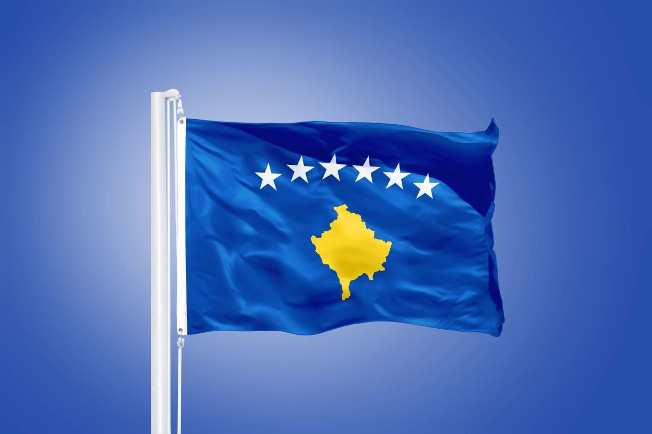 Flag of Kosovo flying against a blue sky.