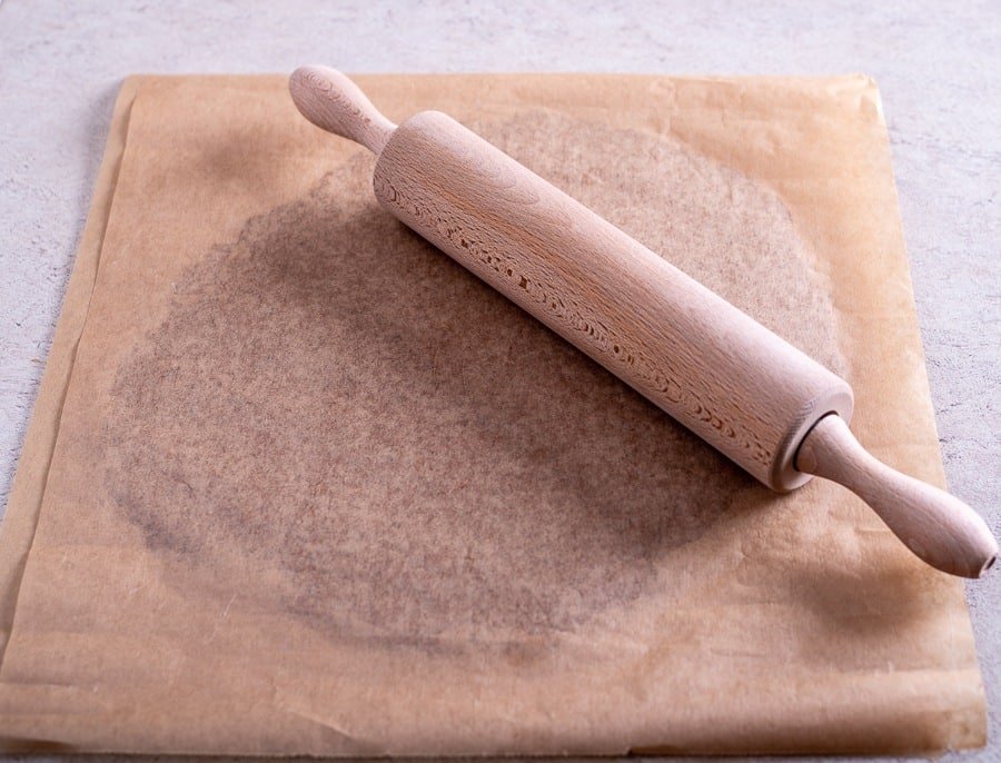 A wooden rolling pin on a piece of parchment paper for rolling out Black Pepper Cookies or Croatian Paprenjaci.