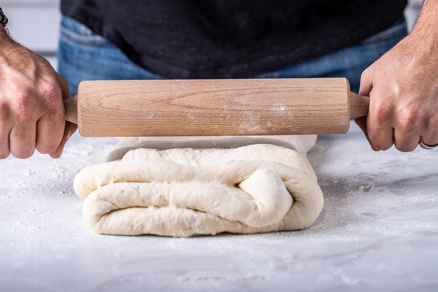 A Croatian man making salenjaci by rolling dough on a rolling pin.