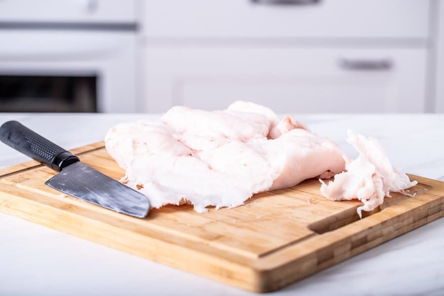 A knife on a cutting board next to a piece of chicken, showcasing the character of Croatian cuisine.