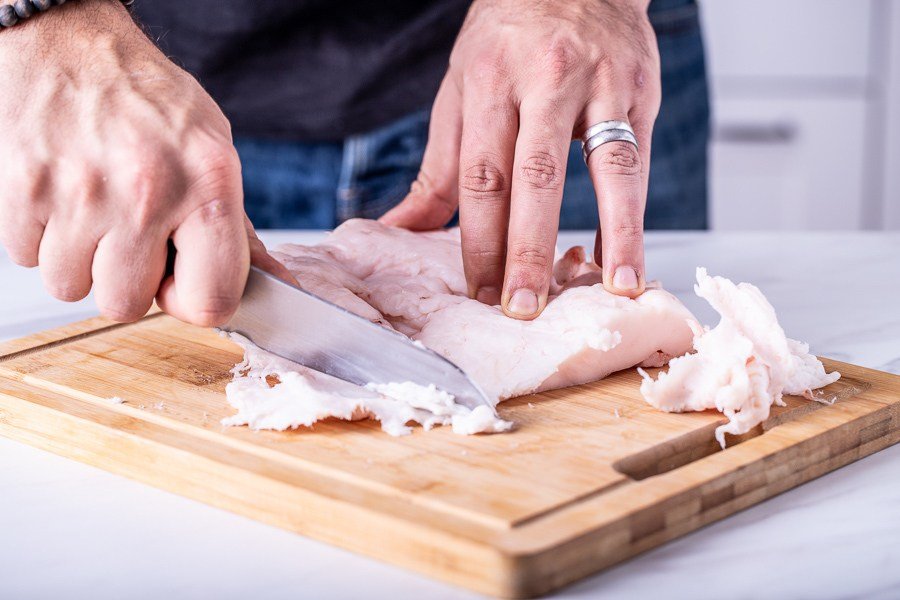 A man is slicing a piece of chicken on a cutting board, while enjoying Croatian croissants.