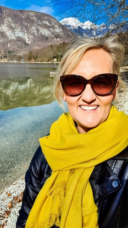 A Slovenian woman wearing sunglasses and a yellow scarf in front of Lake Bled.