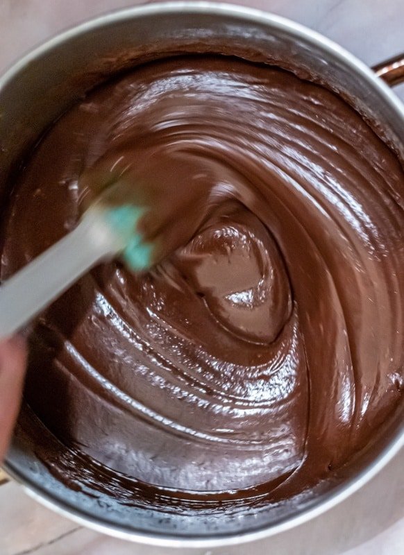 A person making Čokoladnom Karamel Kremom by mixing chocolate in a pan with a spatula.