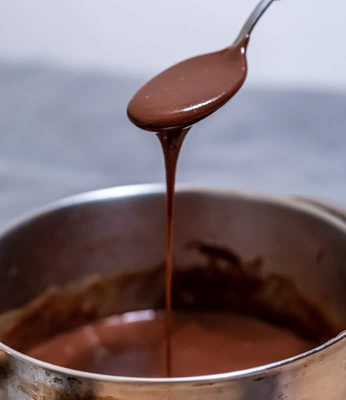 A spoon is pouring Čokoladnom Karamel Kremom into a pot.