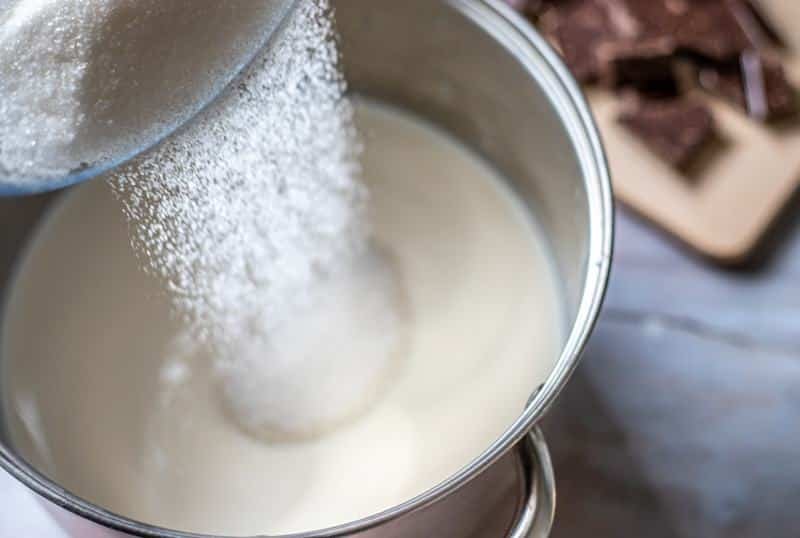 Sugar being poured into a pot of milk while making čokoladnom karamel kremom.
