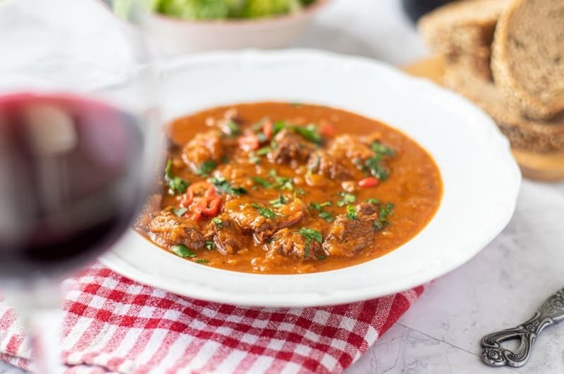 A Traditional Croatian bowl of goulash stew with bread and a glass of red wine.