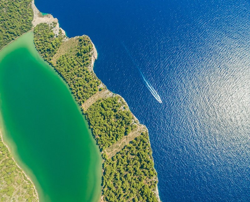 An aerial view of a green lake in the Zadar Region with a boat on it.