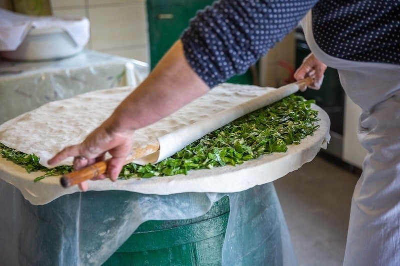 A private woman is making a vegan-friendly pizza with greens on top using Soparnik cooking techniques.