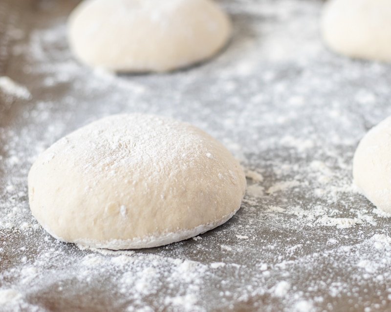 Four dough balls on a baking sheet covered in powder, ready to be baked.