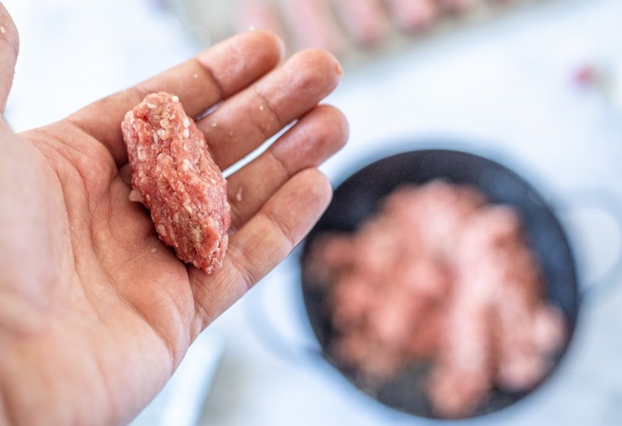 A person's hand holding a piece of Sarajevski Ćevapi in a pan.