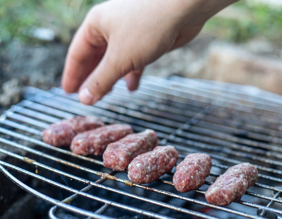 A person is grilling Sarajevski Ćevapi, which are skinless sausages.