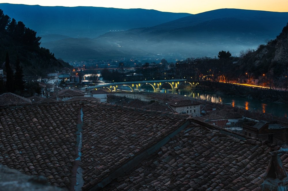 Evening Berat, town is the south of Albania, with its hills, covered with mist, illuminated Gorica Bridge over Osum river and old buildings with tile roofs.