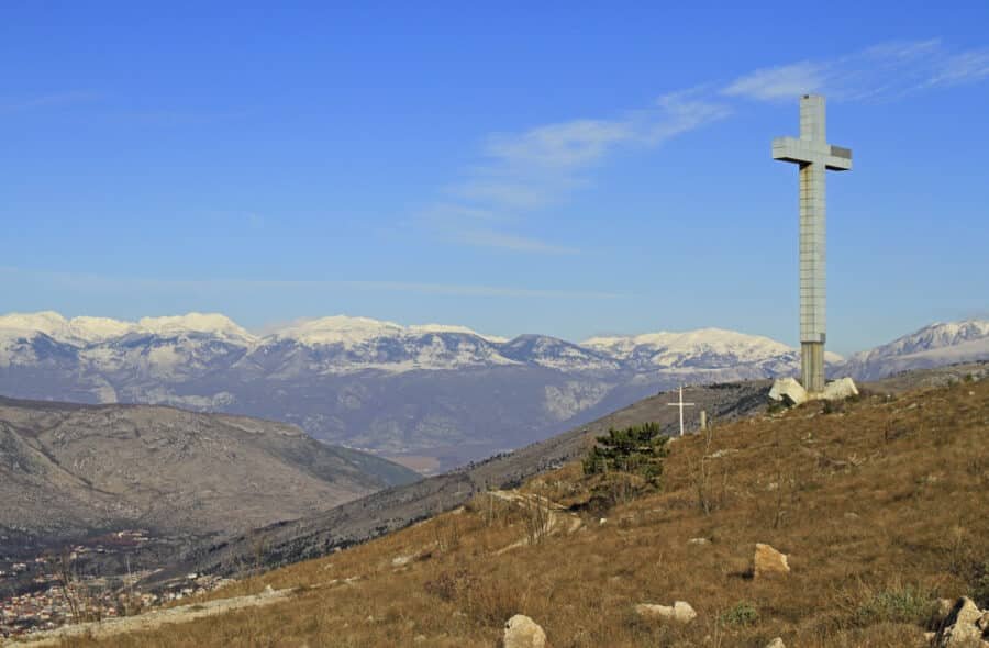 A cross on top of a hill with mountains in the background, taken during 1 day in Mostar.