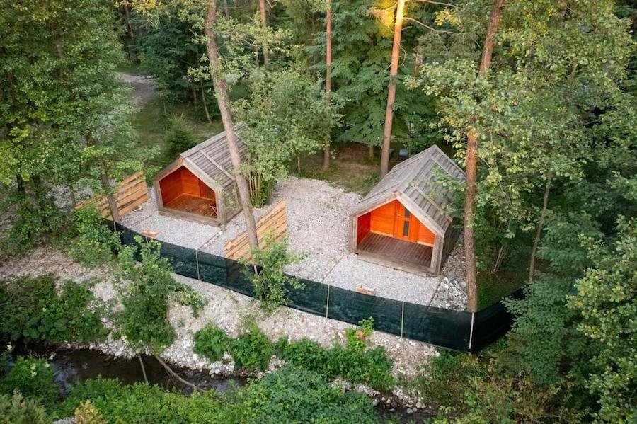 Two wooden cabins in the woods next to a stream, perfect for glamping in Slovenia.