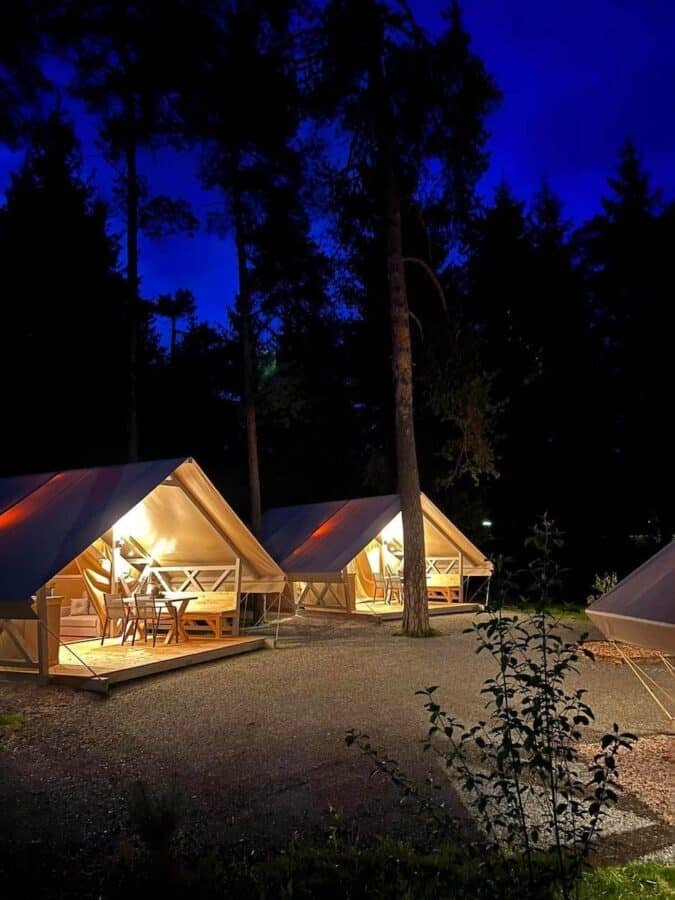 A group of glamping tents lit up at night in a wooded area in Slovenia.