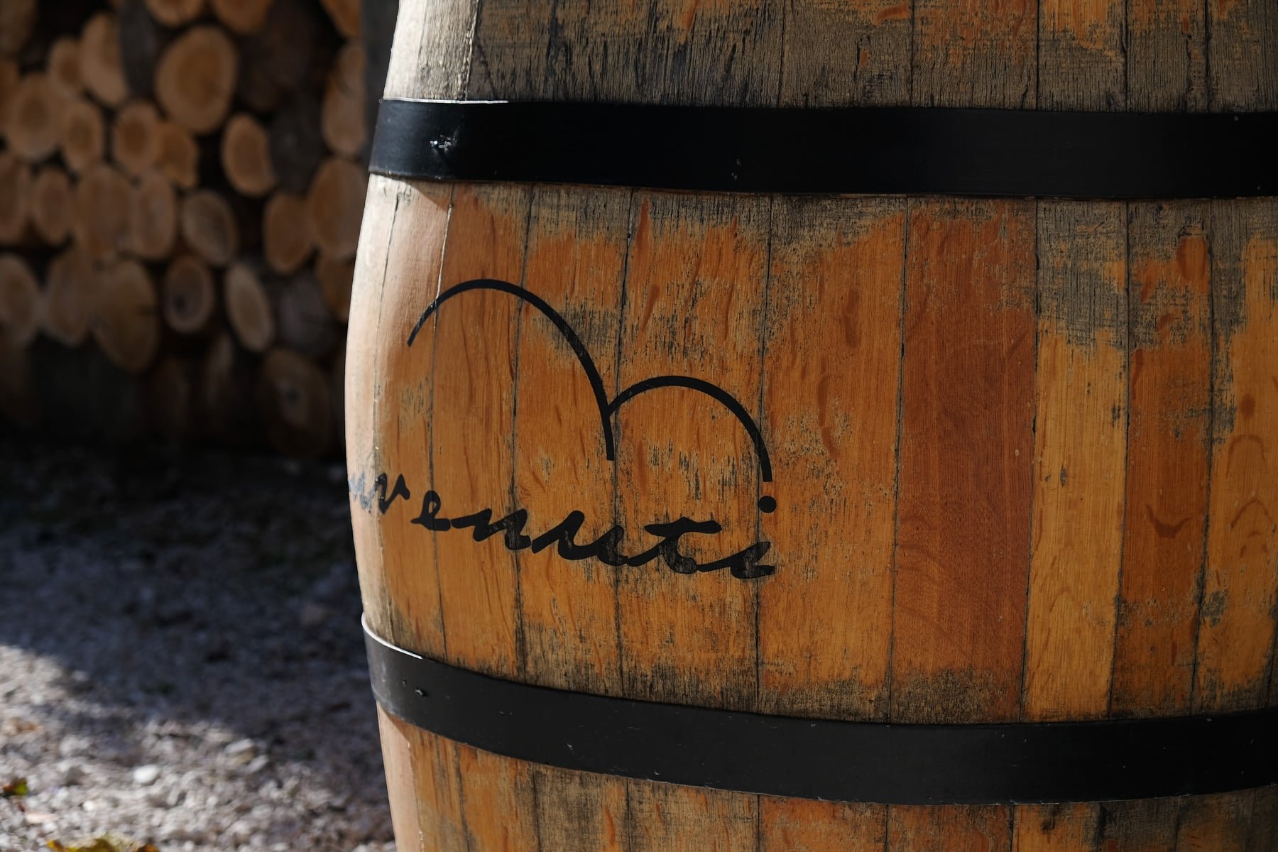 A wooden barrel with the Benvenuti logo on it in front of a pile of logs from Istria at benvenuti Winery, Istria.