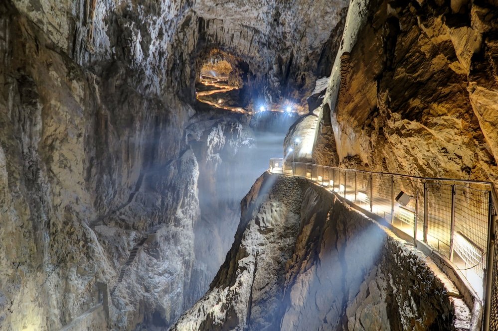 Illuminated walkway inside a spacious Skocjan cave with rock formations and a rugged terrain.