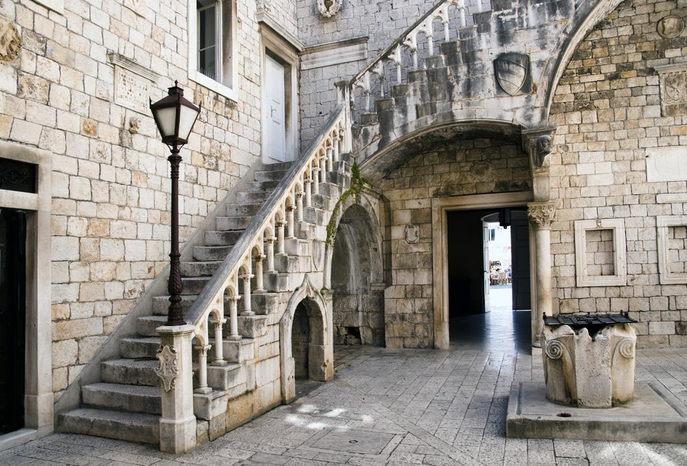 An old stone building (City Hall) in Trogir, Croatia with stairs and a lamp.