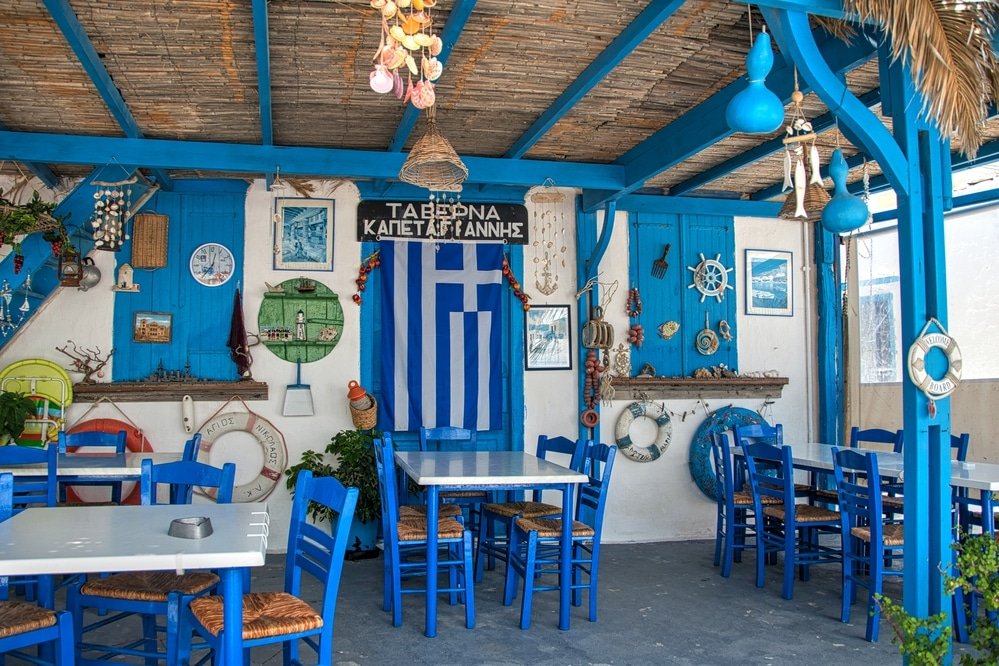 A charming blue and white restaurant nestled on Karpathos Island in Greece, offering an inviting ambiance with its wooden tables and chairs.