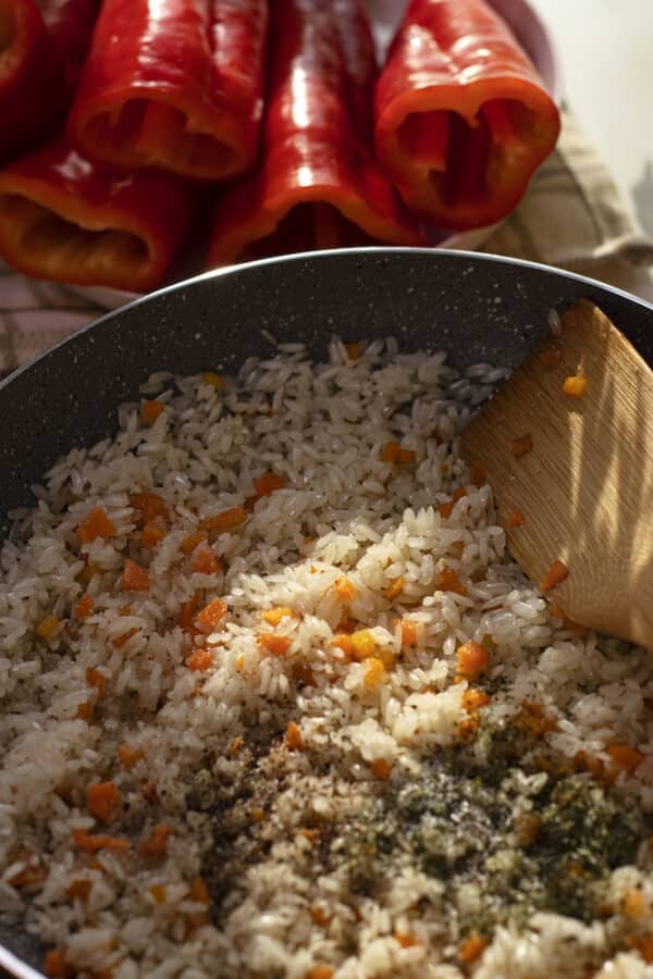 Vegetarian-friendly Palneni Chushki cooked with rice and peppers in a pan, stirred with a wooden spoon.