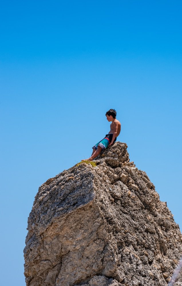In Kythira, Greece, a boy finds solace sitting on top of a rock on kaladi beach in Kythira island,