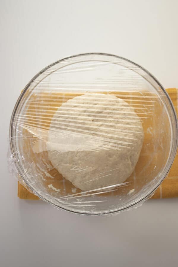 A Bulgarian recipe of mekitsi, a bowl of dough wrapped in plastic on a table.