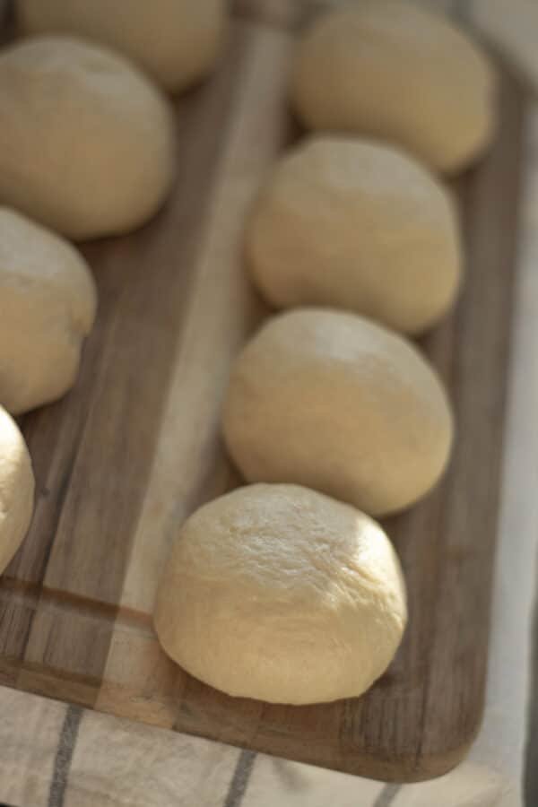 A wooden cutting board with several Bulgarian dough balls, known as Mekitsi, on it.