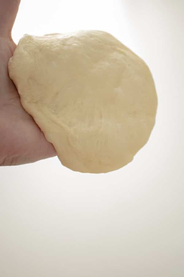 A Bulgarian person's hand holding a piece of dough for the traditional recipe of Mekitsi.