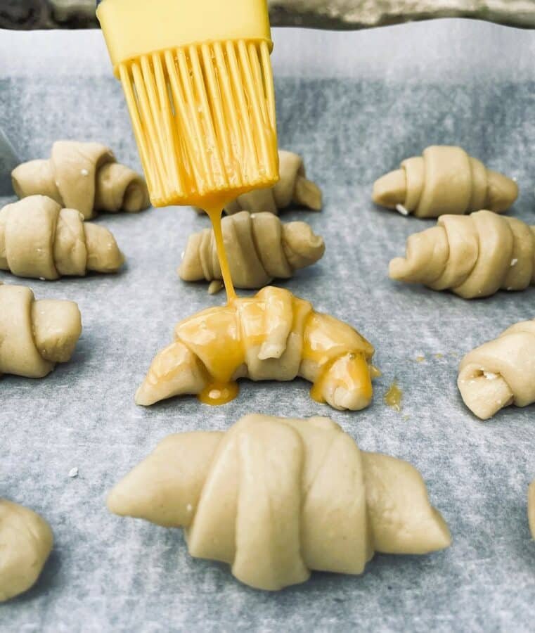 A yellow cheese is being poured onto a baking sheet of crescent rolls.