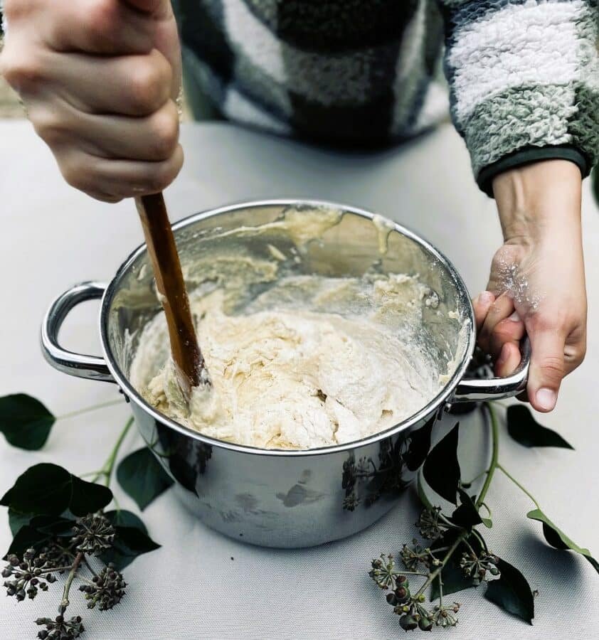 A person stirring a bowl of batter with a wooden spoon while preparing a recipe.