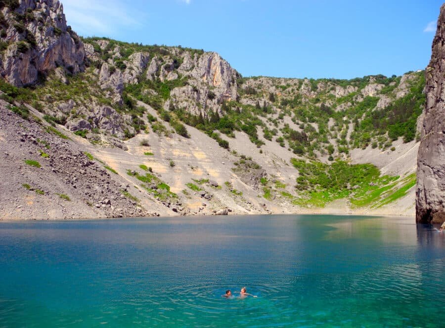 Two people swimming in a lake near a rocky cliff in Imotski, Croatia.