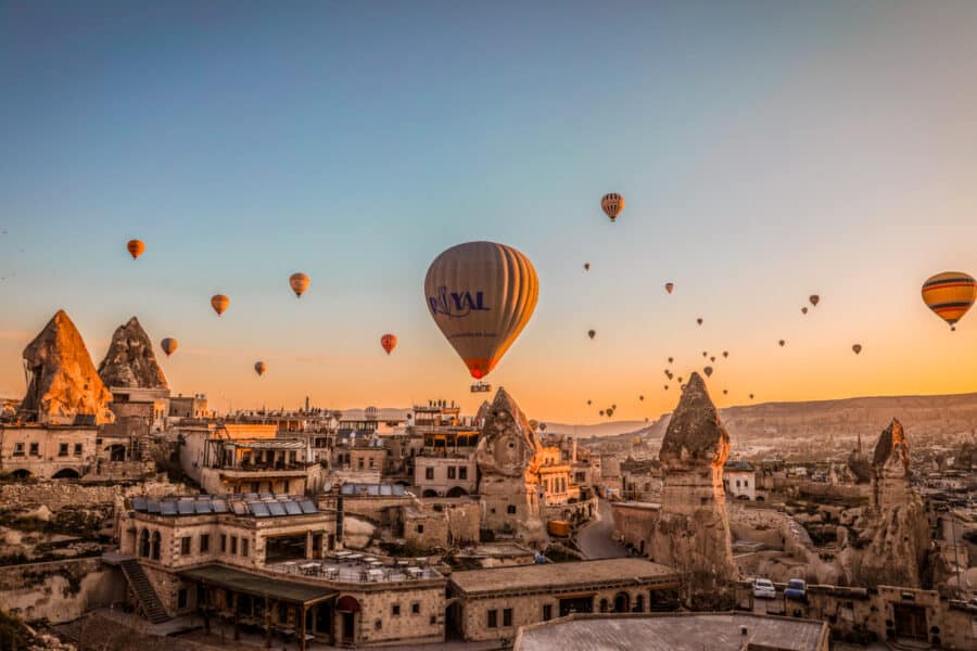 Hot air balloons floating over Cappadocia's rocky landscape at sunrise, with historic cave dwellings visible.