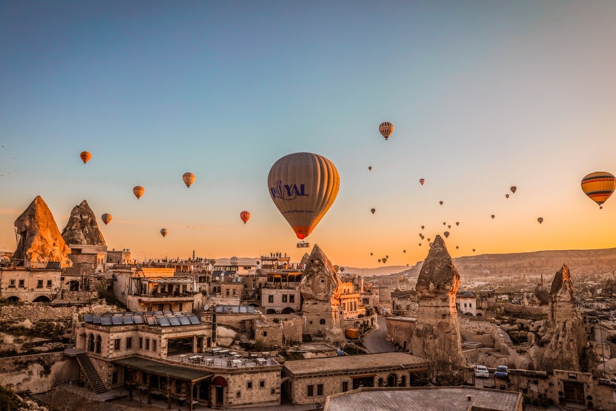 Hot air balloons float over the unique rock formations and structures of Cappadocia, Turkey, during a golden sunrise.