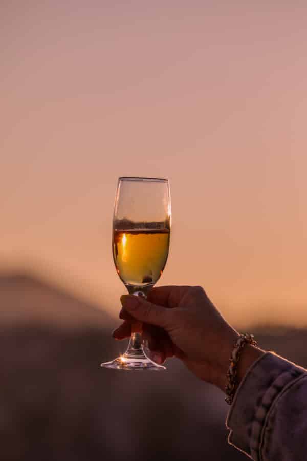 A hand holding a glass of white wine against a Cappadocia sunrise with soft focus mountains in the distance.