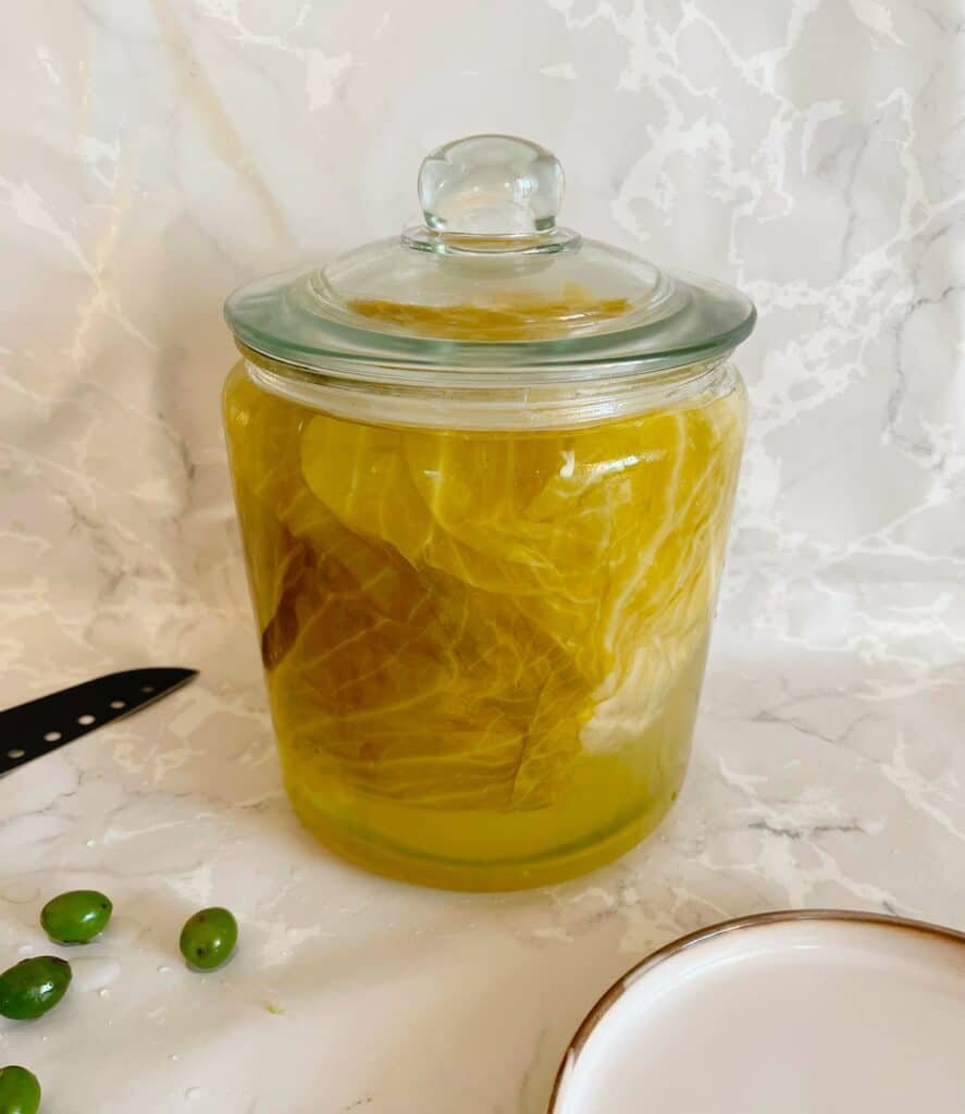 A glass jar filled with sour cabbage leaves and a knife.