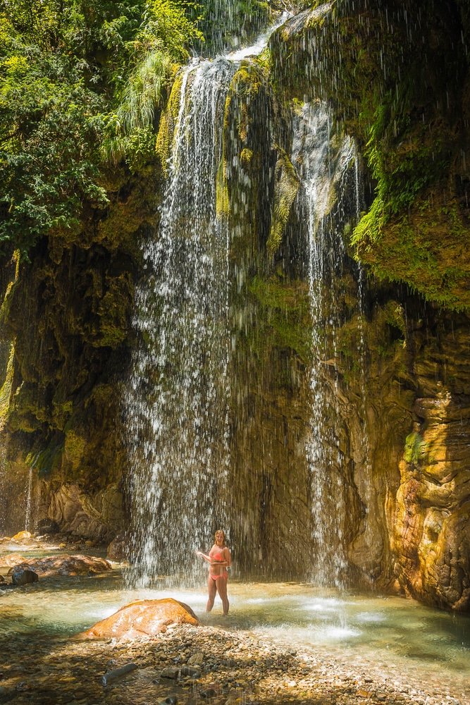 A girl standing in front of a waterfall in Central Greece, experiencing the beautiful Greek Life at Panta Vrechei Gorge
