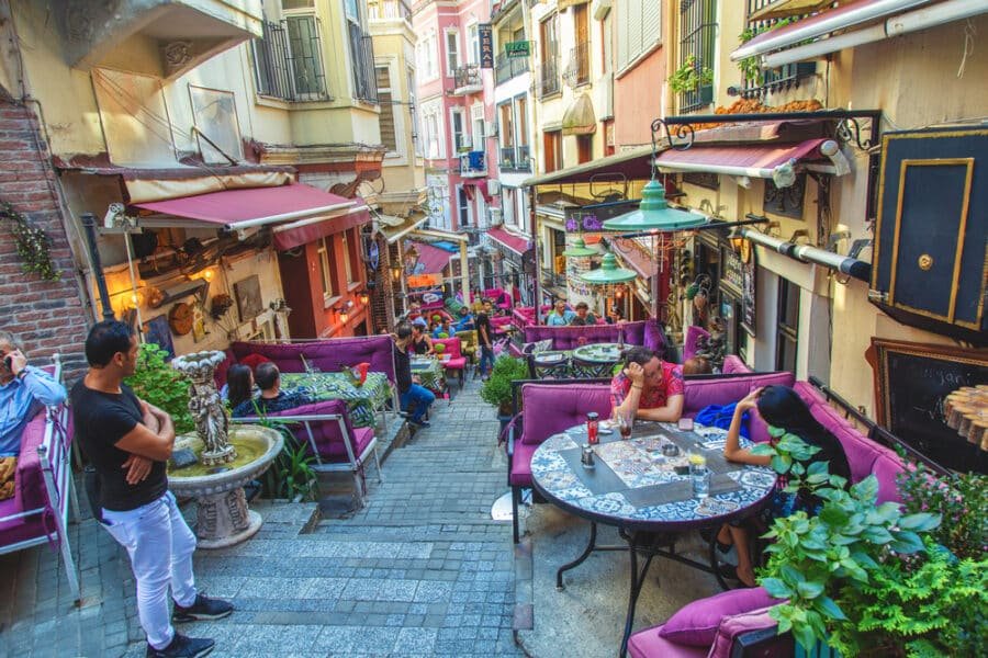 People are sitting at tables in a narrow alley in Beyoglu, Istanbul.