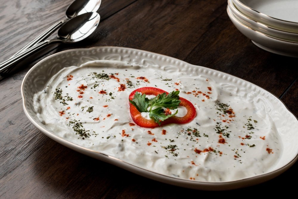 Turkish Appetizer Haydari with yogurt (Tzatziki) in white plate on wooden surface.