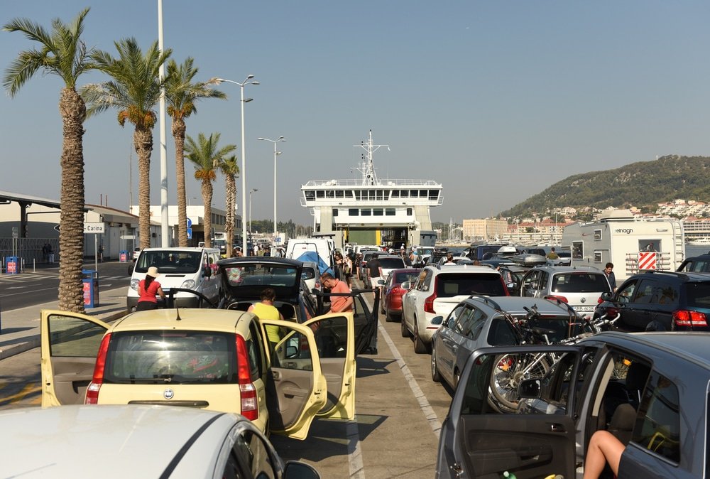 Ferry From Ancona To Split Guide - A group of cars parked on a road with a ferry in the background at Split going to Ancona.