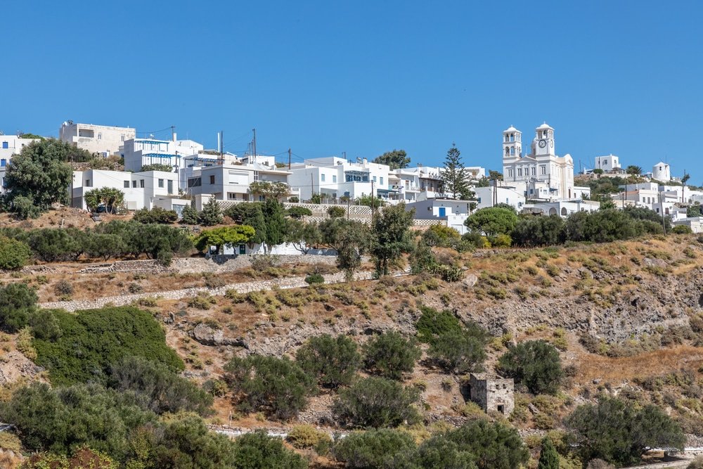 Houses and church in Trypiti village, Milos, Greece. Featuring charming white buildings nestled among lush trees.