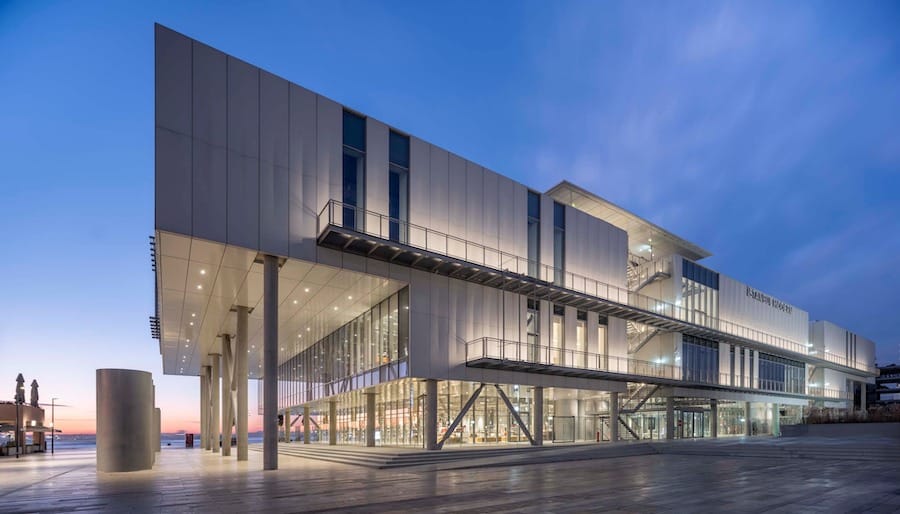 Modern building with glass and metal facade, large overhangs, and elevated sections at dusk. The sky is a gradient of blue and purple, reflecting the vibrant life of Istanbul. The building is well-lit from inside, perfect for families enjoying an evening with their kids.