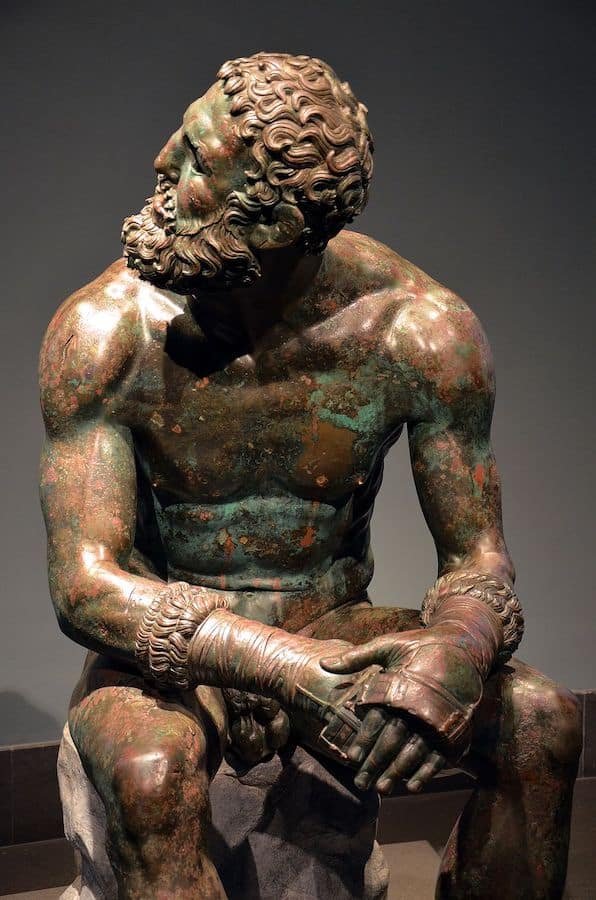 A famous bronze statue of a man sitting on a rock, resembling Greek statues.