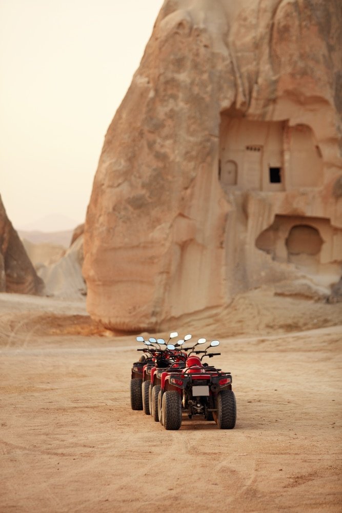 Four atvs parked in front of a rock formation in Cappadocia.