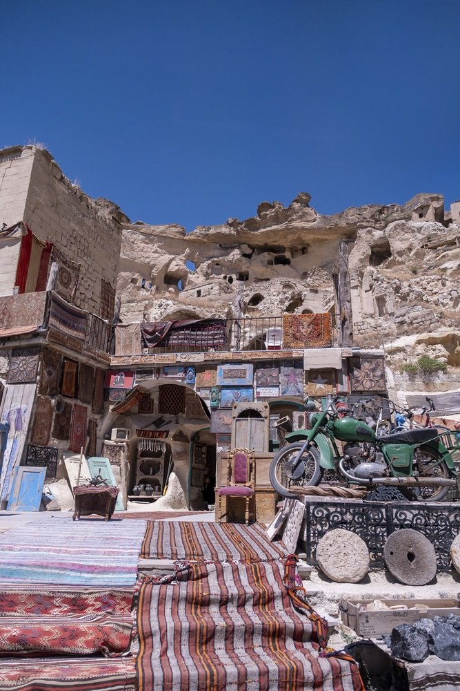A motorcycle is parked in front of a house with rugs on the ground. Nearby, in Cappadocia, there are exciting ballooning activities to do.