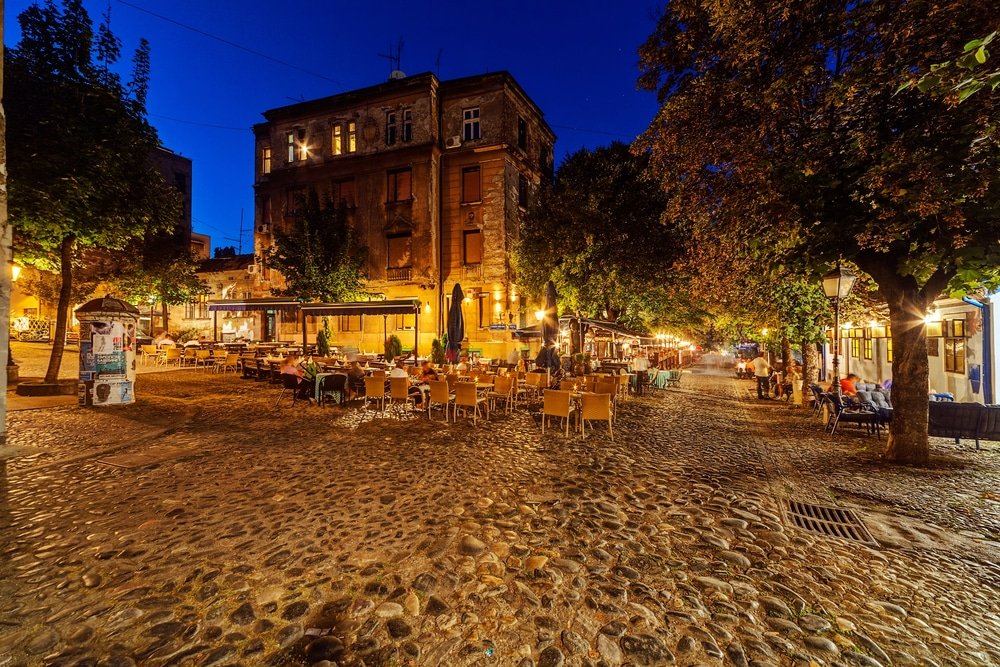 Skadarlija street in Belgrade, Serbia, with tables and chairs and trees in the background.